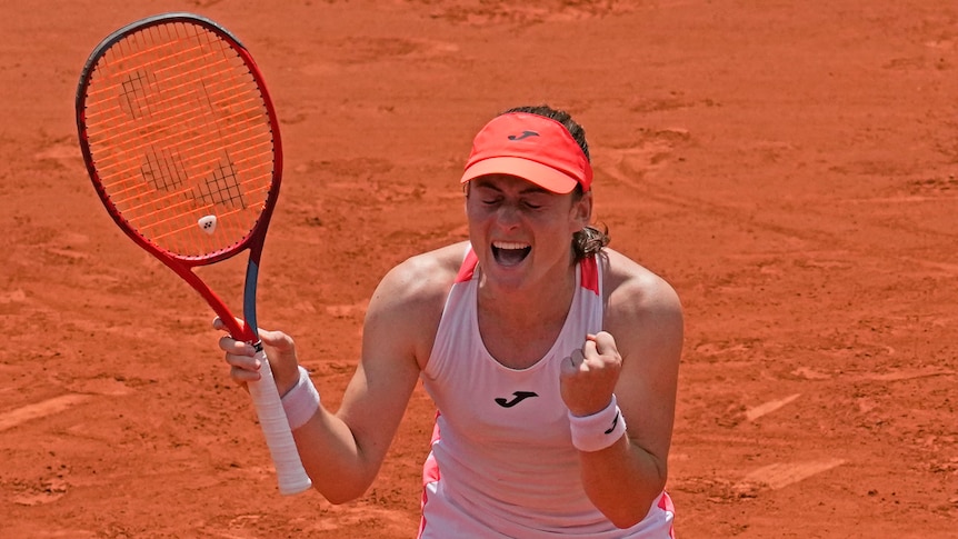 A female tennis player closes here eyes, clenches her fist and shouts in celebration after winning a match.