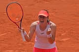 A female tennis player closes here eyes, clenches her fist and shouts in celebration after winning a match.