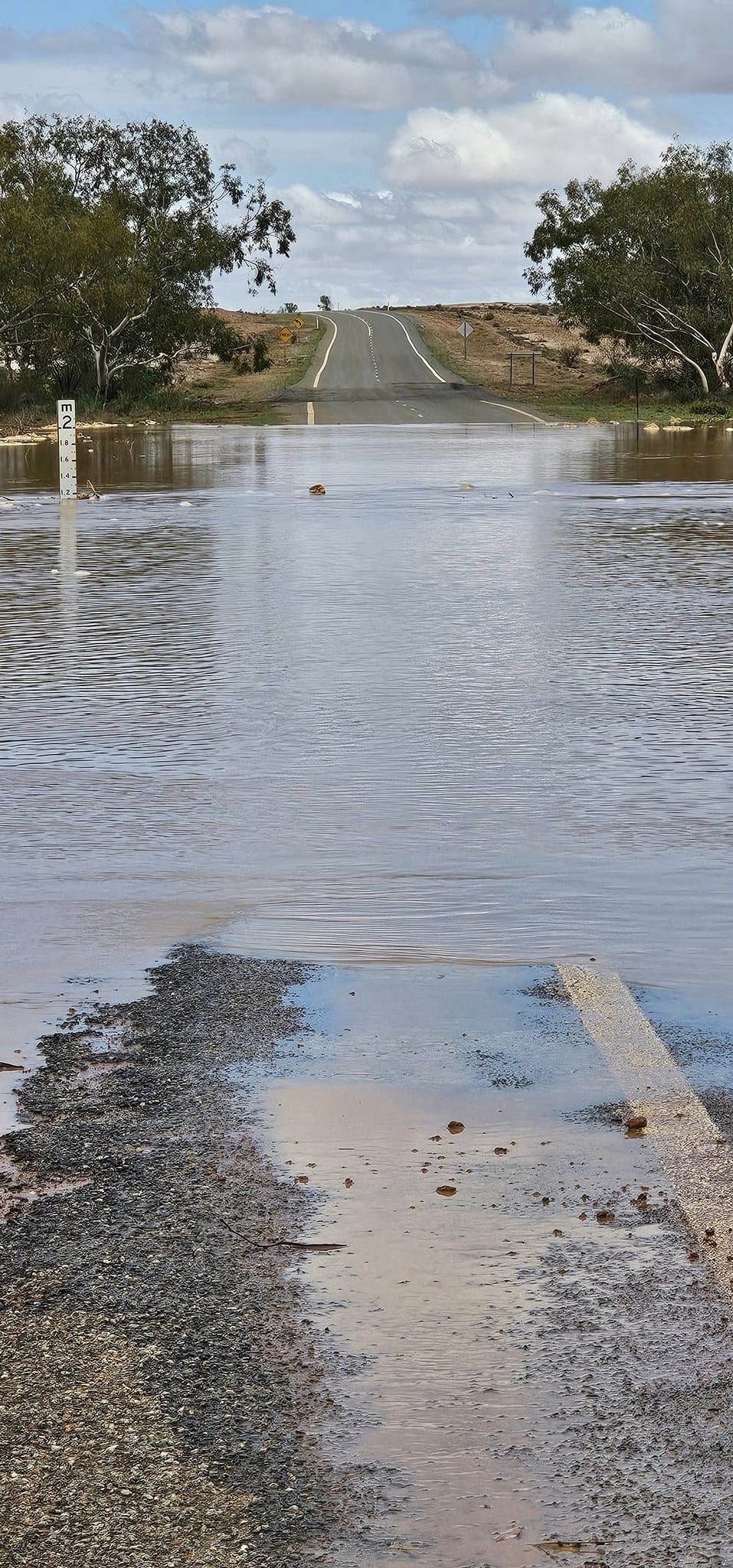 A large body of water covering a road with a flood indicator showing the level is above one metre
