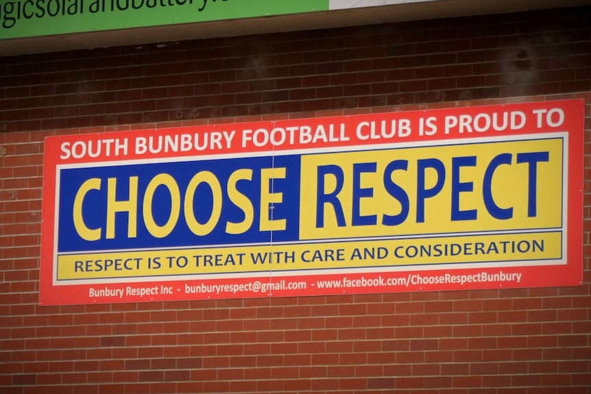 A yellow and red football club sign attached to a brick wall