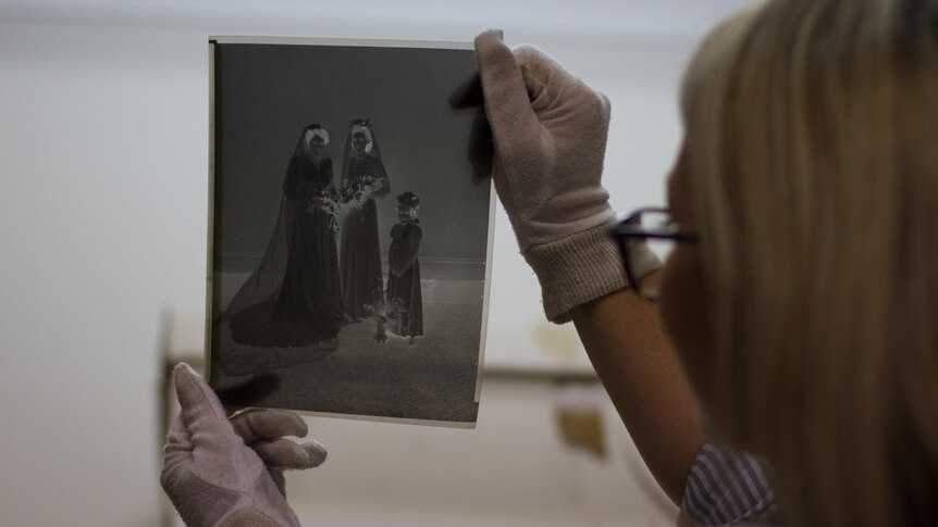 A woman wearing white gloves holds up the negative of a historic photograph to the light.