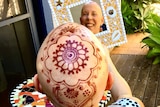 A bald woman with an intricate henna crown smiles into a mirror.