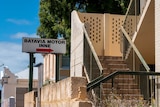 A sign says 'Batavia Motor Inne' with an arrow that points to a run down staircase to enter the motel. The sky is blue.
