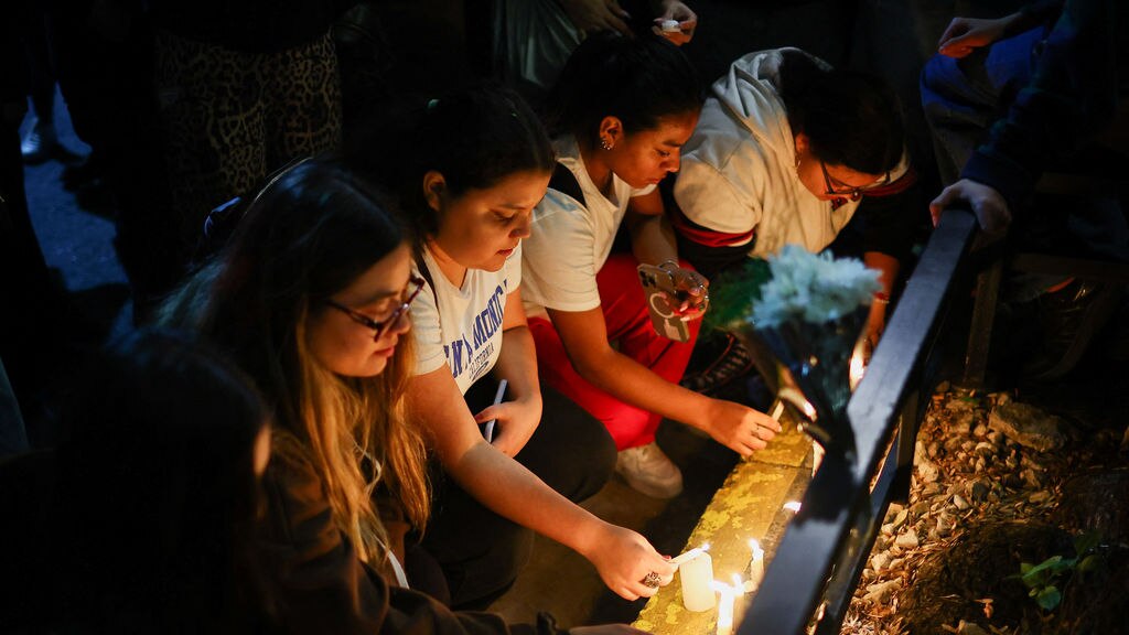 People kneel down lighting candles and placing flowers at a vigil.