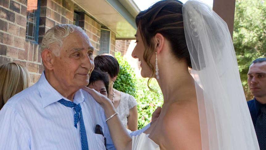 A bride smiles as she puts her hand on her grandfather's shoulder. He looks proud