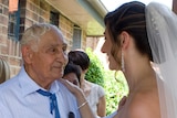 A bride smiles as she puts her hand on her grandfather's shoulder. He looks proud