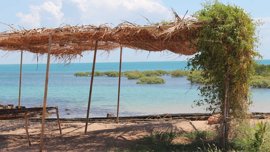 Crystal clear blue ocean with straw hut or tent like structure on the shore.