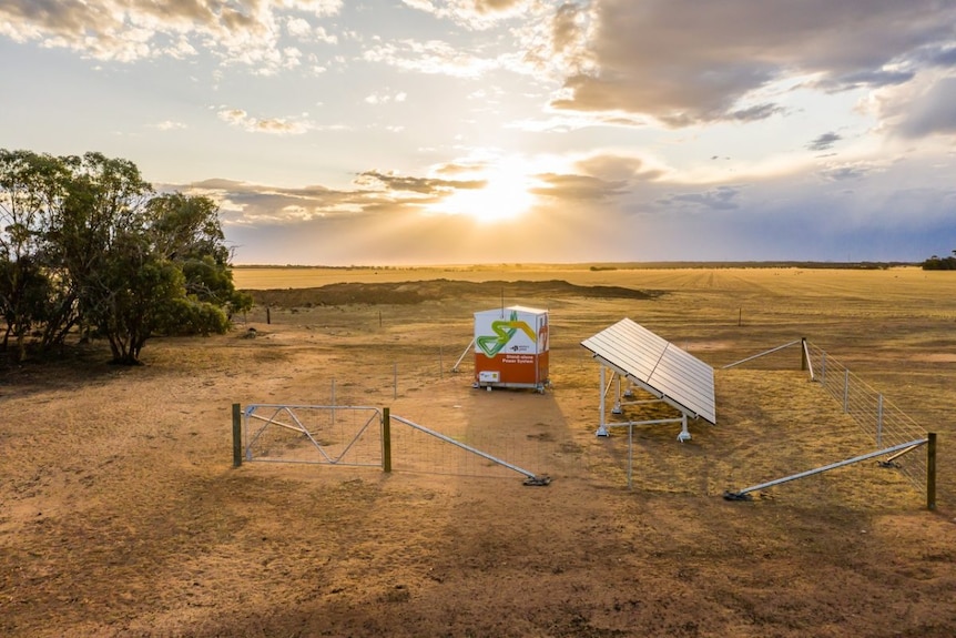 A row of solar panels and a metal box in a flat and sunny landscape