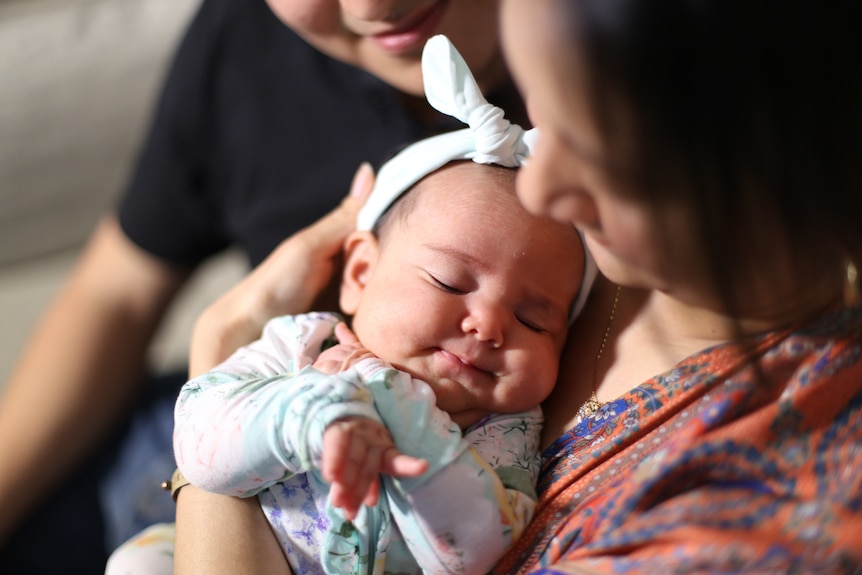 A mother holds a baby with a bow on its head in her arms