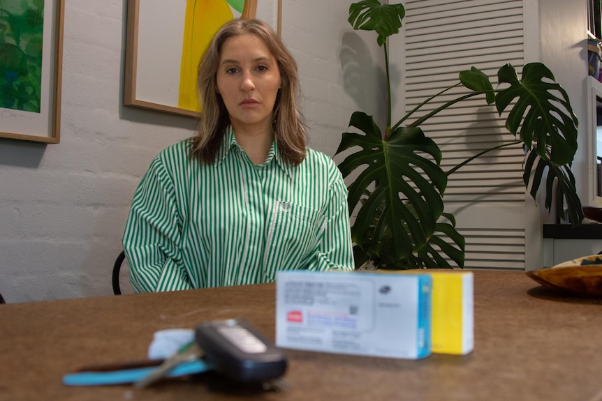 A set of car keys and medication boxes close to camera, with a woman sitting in the background