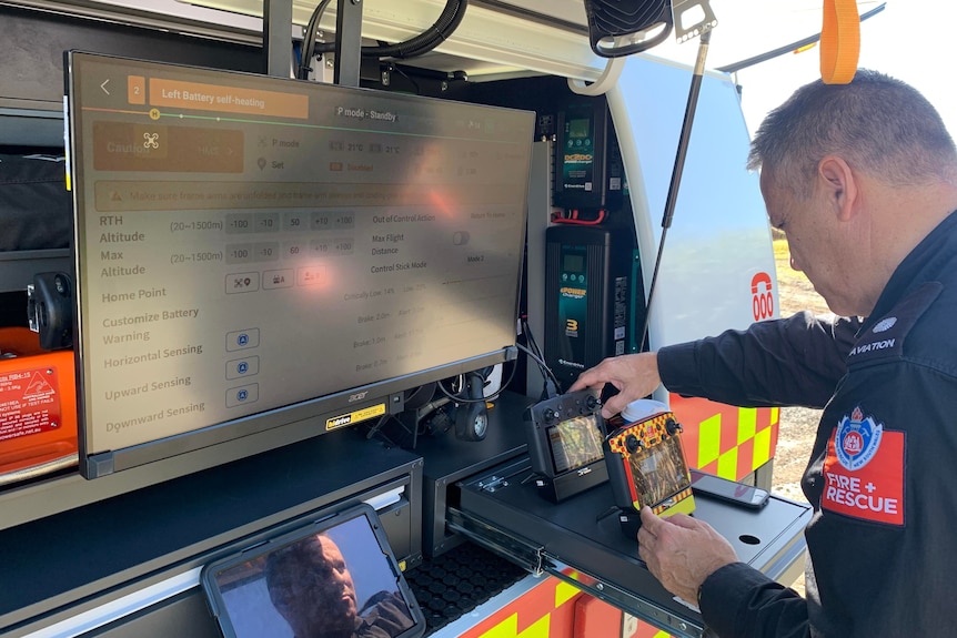 A man in fire and rescue nsw uniform looks at digital screens on the back of a truck.