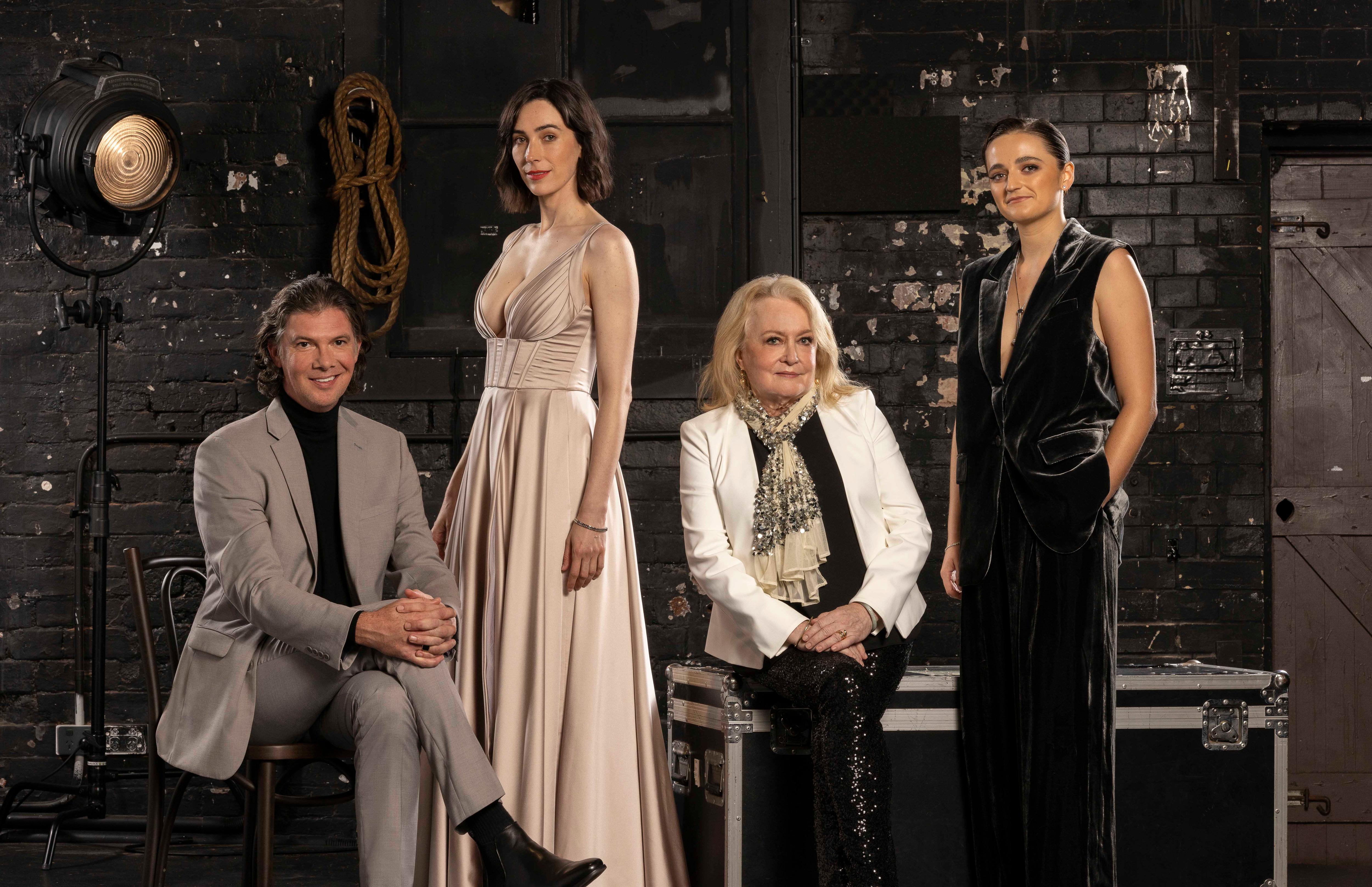 A white male actor and three white female actors stand wearing formal attire inside a theatre.