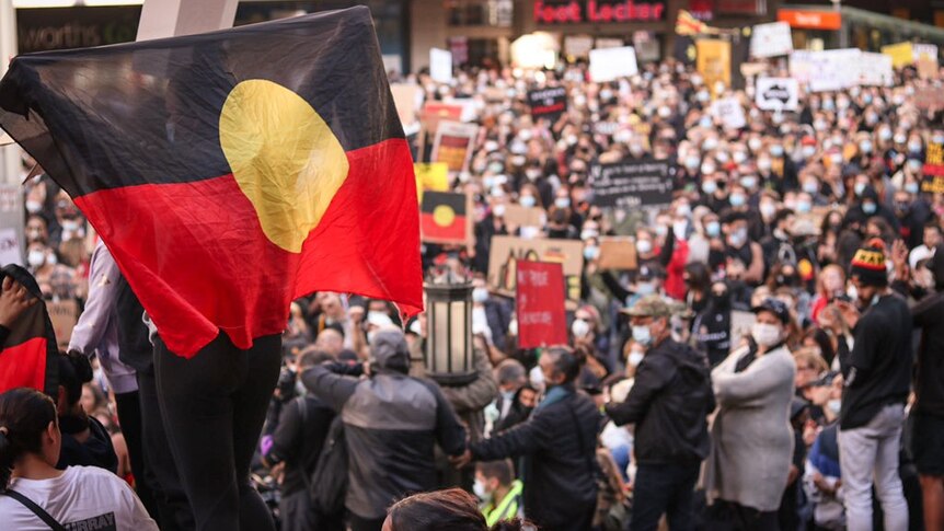 An Aboriginal flag is waved in a huge crowd of people in Sydney's CBD