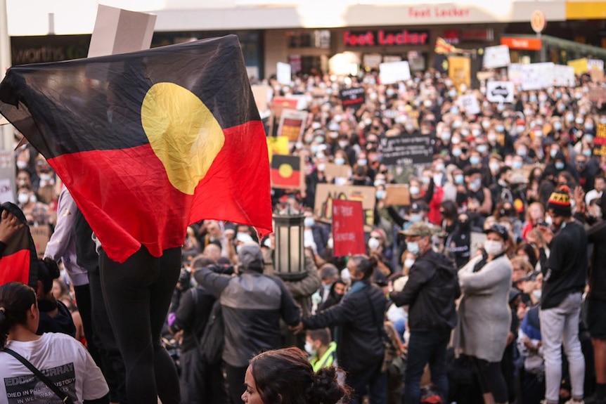 An Aboriginal flag is waved in a huge crowd of people in Sydney's CBD