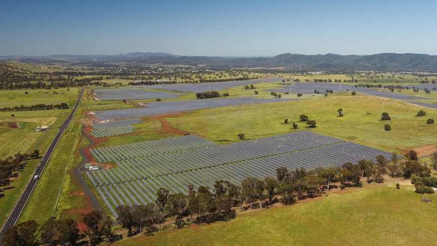 A drone shot of a massive solar farm, green paddocks and hills in the distance.