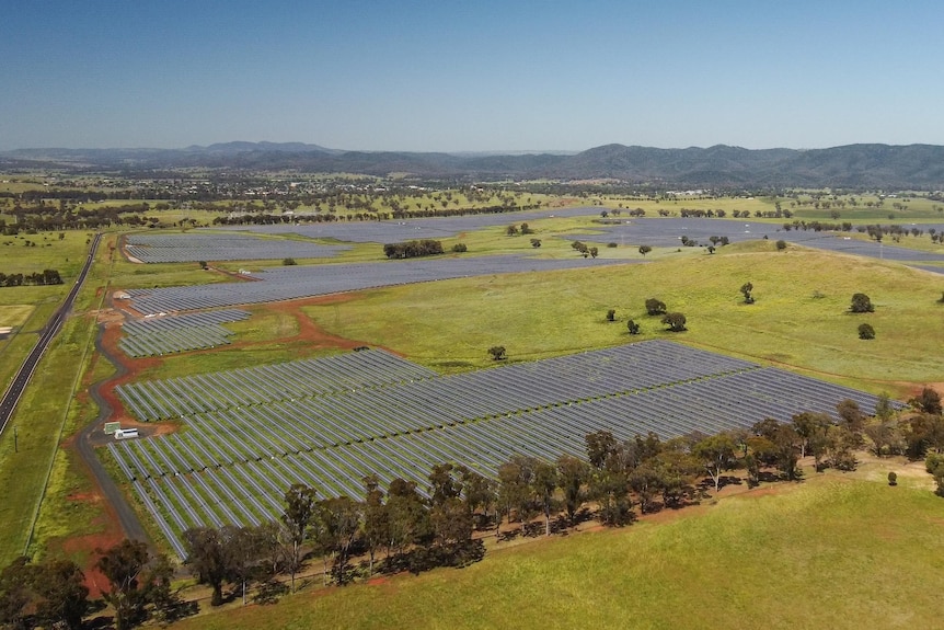 A drone shot of a massive solar farm, green paddocks and hills in the distance.