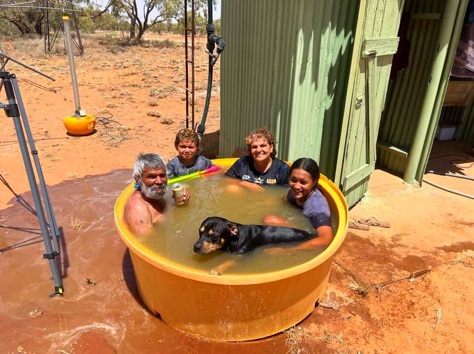 Three adults, a child and a dog in a small children's pool.