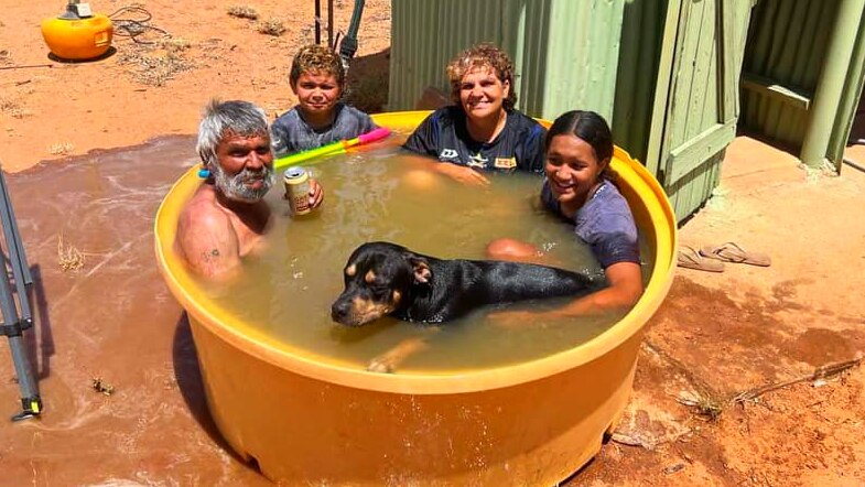 Three adults, a child and a dog in a small children's pool.