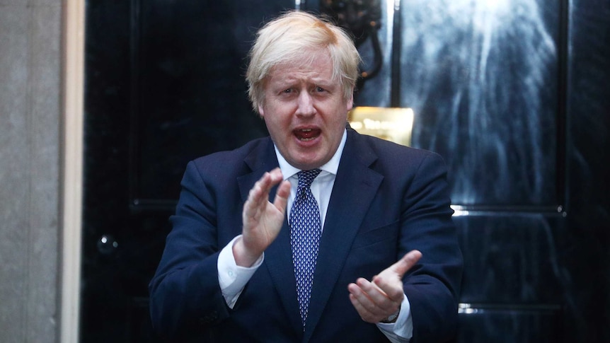 Boris Johnson claps while standing outside a front door