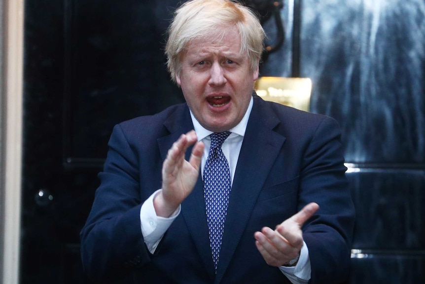 Boris Johnson claps while standing outside a front door