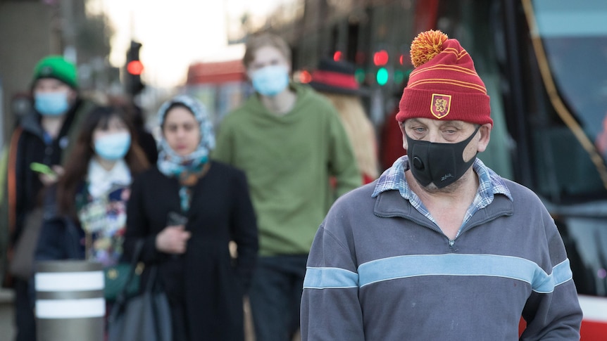 A man wearing a red beanie walks with a facemask on 