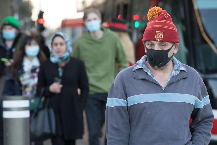 A man wearing a red beanie walks with a facemask on 