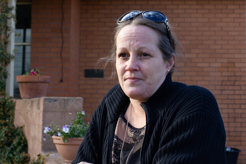 A woman leans on a brick wall and looks into the distance.