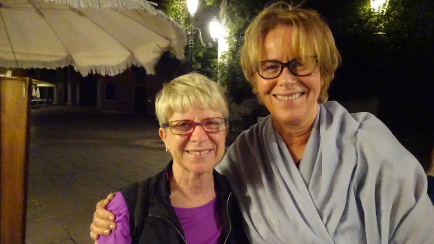 Two women posing for a photo at night with street lights and greenery in the background.