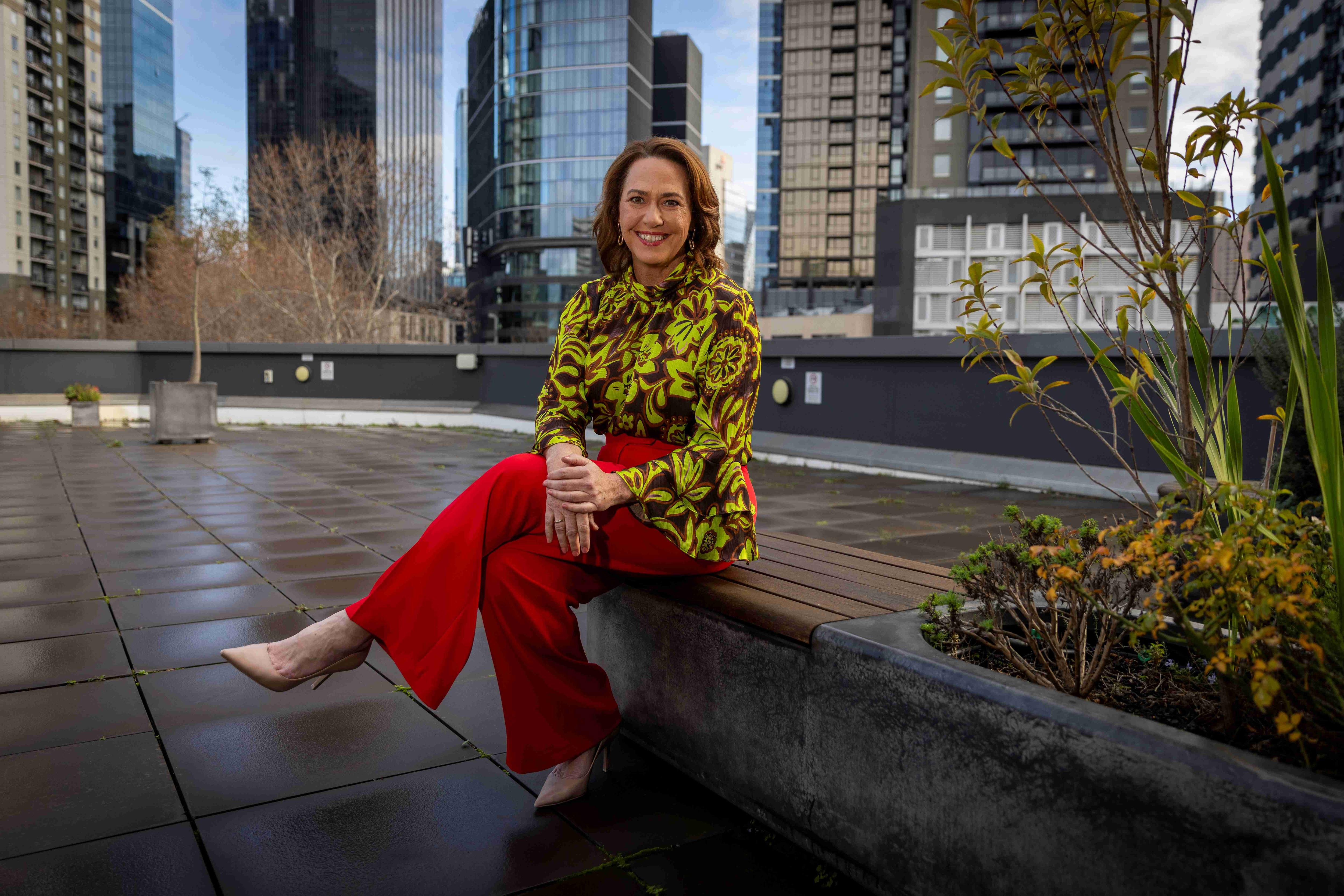 Lisa Millar sitting besides some plants in a city landscape.