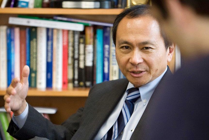 A man gestures in front of a bookcase