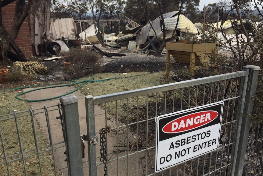 Destroyed property with sign on the gate saying "Danger asbestos, do not enter".