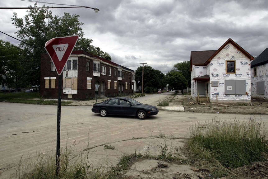 A car drives past abandoned houses in Detroit