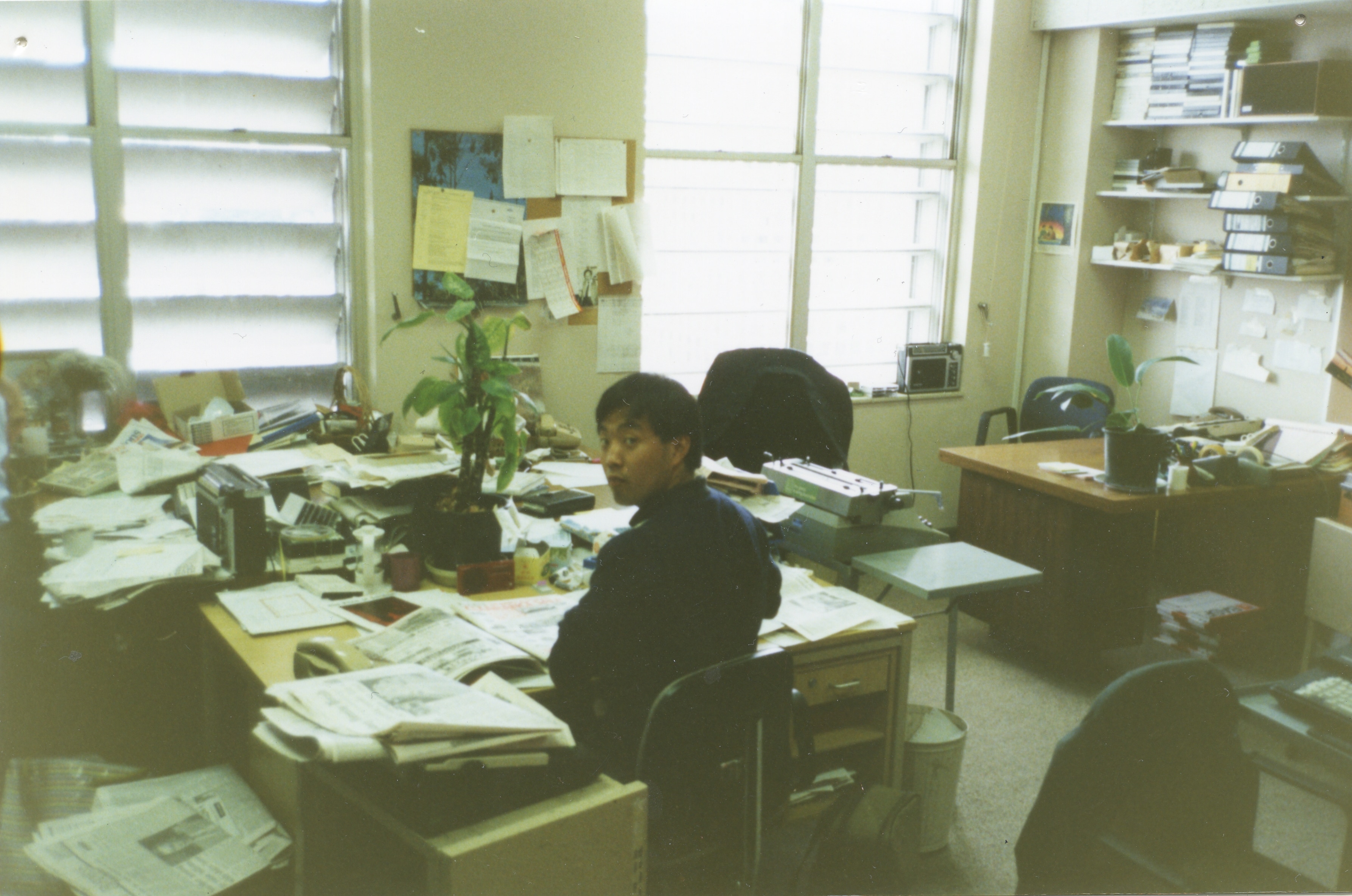 a sepia toned film photo of a man at a busy desk