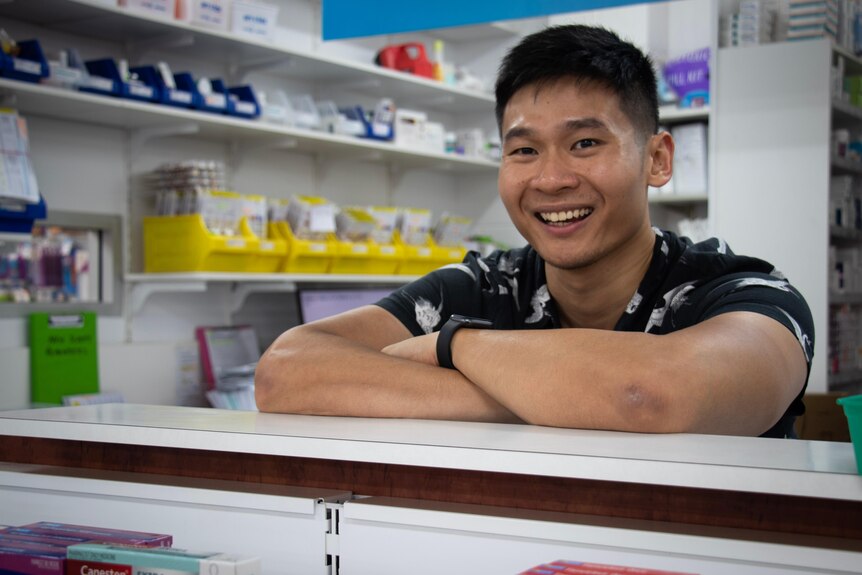 Portrait of a young pharmacist with medication shelves behind him.