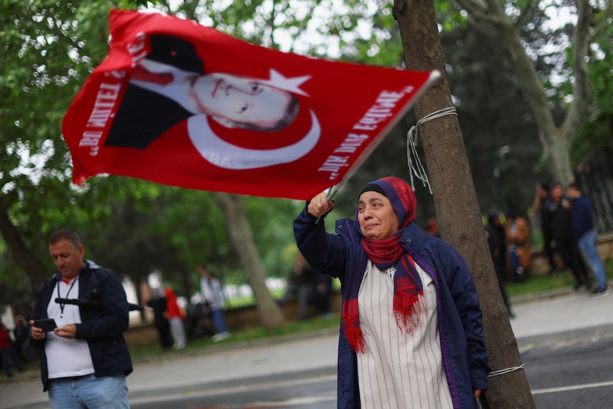 A woman cries waving a flag showing Turkish President Tayyip Erdogan's face.