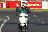 F1 driver Sebastian Vettel waves with both hands as he rides a scooter on the Australian Grand Prix track.