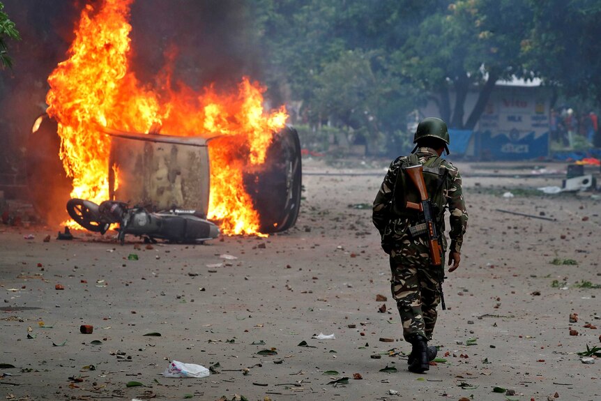 A military person walks towards a burning car.