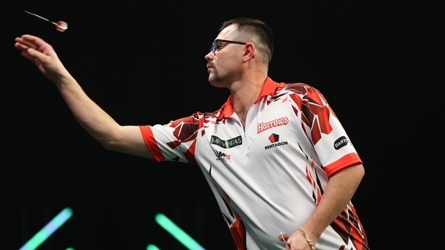 side view of a man in a white and red shirt and glasses throwing a dart