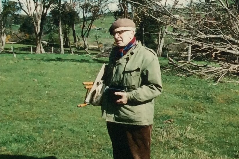 Man standing in field with art easel in hand