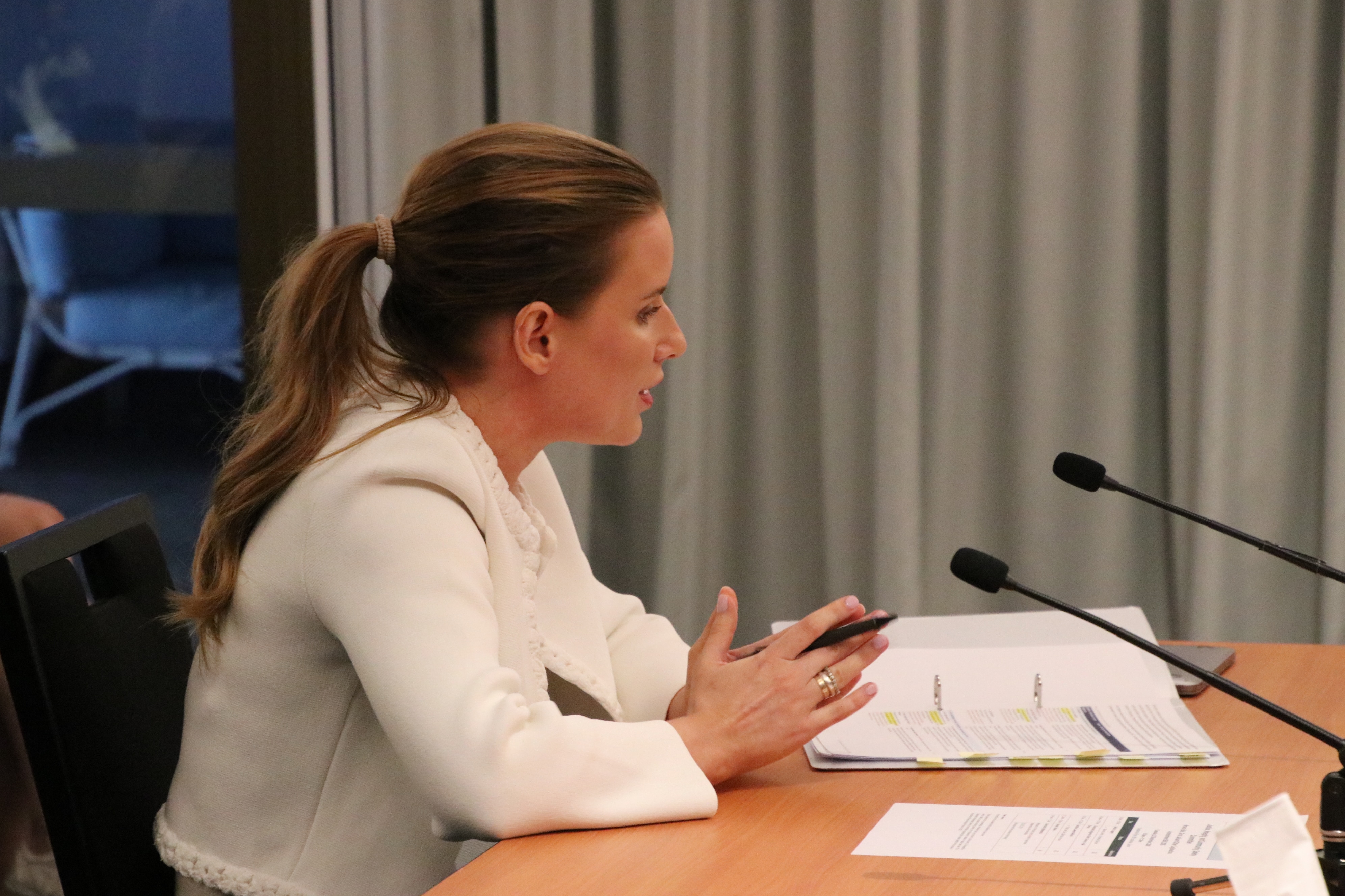 A woman in a white suit talking into a microphone on a table.