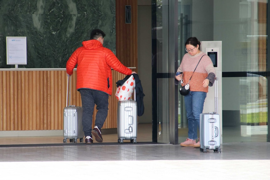 Two people wheeling suitcases into a lobby.