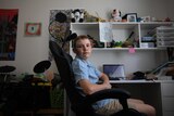 teenager sits at desk in front of computer in a bedroom
