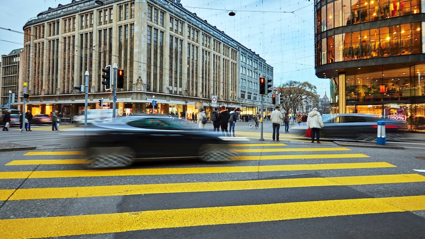 A city intersection with the blurred shapes of cars crossing a marked pedestrian crossing