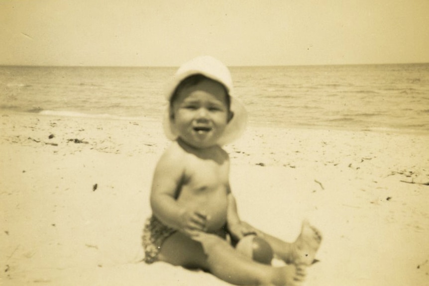 Black and white photo of a baby wearing a hat on the beach.