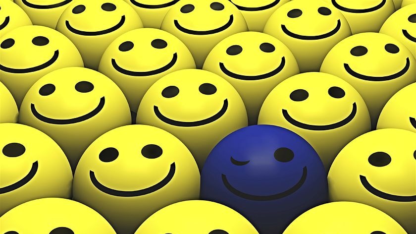 A computer generated image of a group of yellow smiley faces with a blue winking face in the centre.