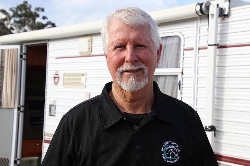 A head and shoulders shot of grey nomad Ian Baird standing in front of his caravan posing for a photo smiling.