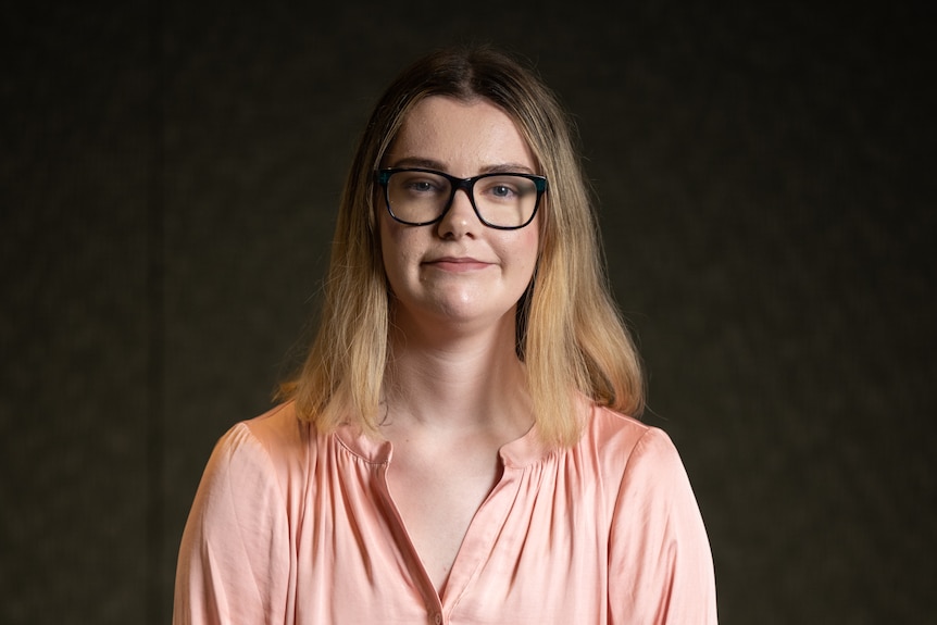 woman in pink shirt with glasses standing in front of black wall