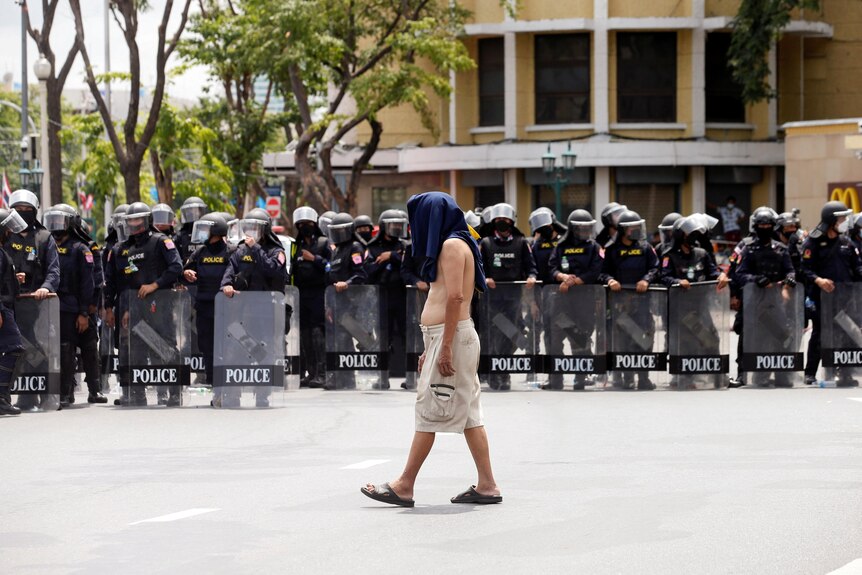 A lone protester walks calmly in front of a line of police in Bangkok during the protest