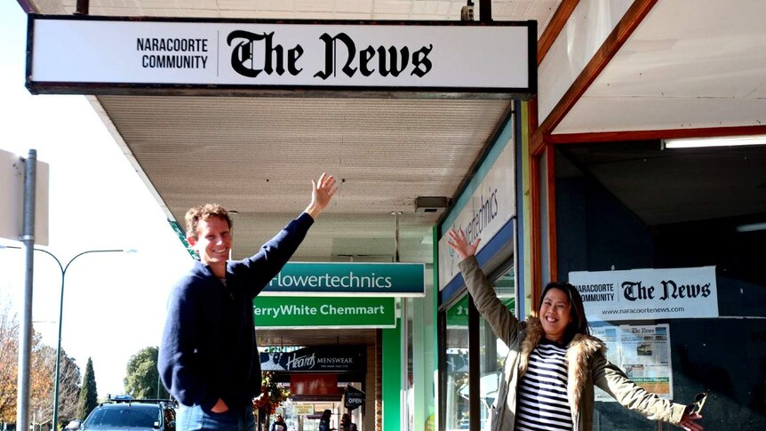 Michael Waite smiles standing under a hanging sign reading 'Naracoorte Community 'The News'.