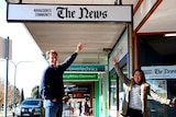 Michael Waite smiles standing under a hanging sign reading 'Naracoorte Community 'The News'.